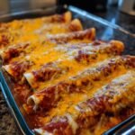 Close-up of freshly baked Pizza Enchiladas covered in bubbling red sauce and melted orange cheddar cheese in a glass baking dish.