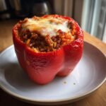 A single, bright red, baked Sausage Stuffed Peppers, topped with melted cheese, sitting on a white plate.