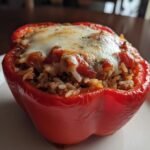 A close-up of a bright red, baked Sausage Stuffed Pepper filled with rice and meat, topped with melted mozzarella cheese and sauce.
