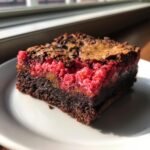 A rich, fudgy square of Strawberry Crunch Brownies featuring a bright pink, textured topping on a white plate.