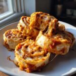 A stack of freshly baked Tortilla Pizza Rolls covered in melted, stringy mozzarella cheese and pizza sauce.